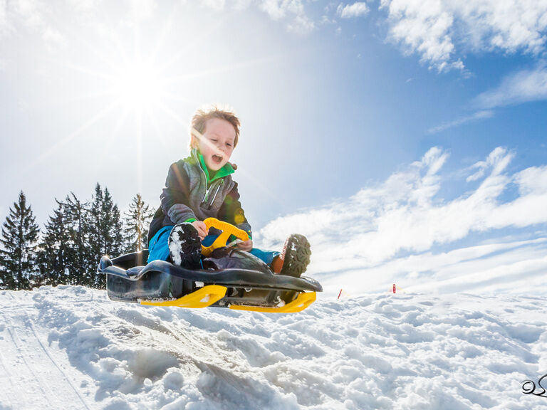 Junge schanzt mit Bob über Schneehügel und juchzt vor Freude
