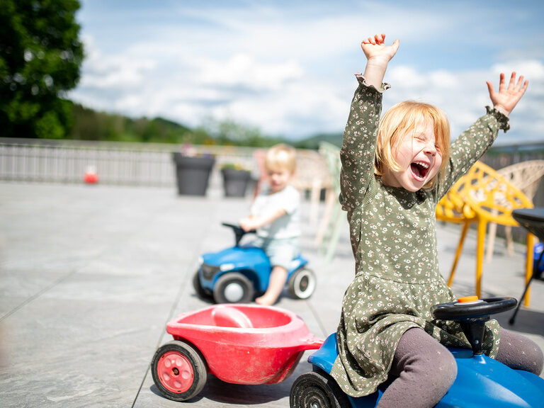 Kind auf Bobbycar auf der Terrasse