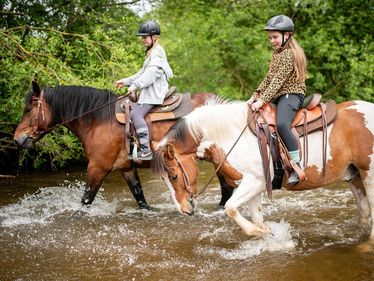 2 Mädchen auf Pferden im Bach