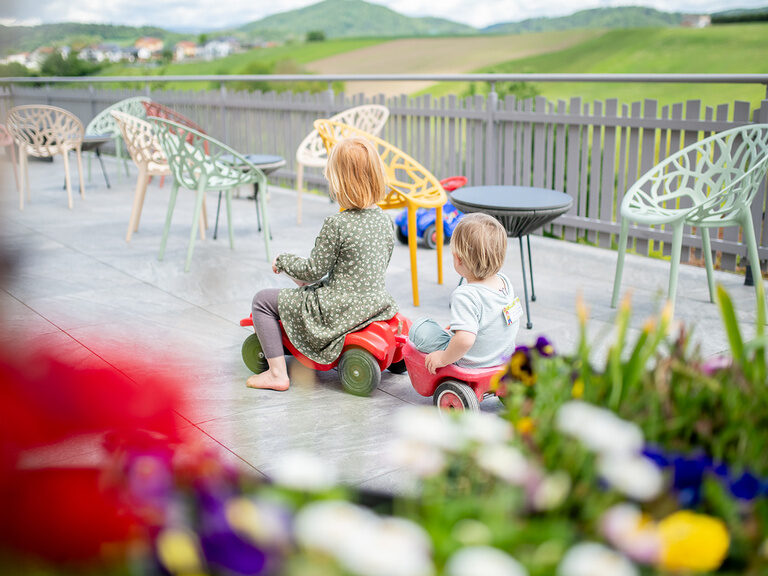 2 Kinder auf Bobbycar auf der Terrasse
