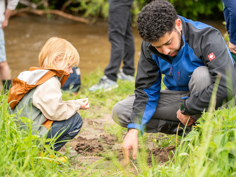 Kind und Kinderbetreuer untersuchen etwas im Bachbett