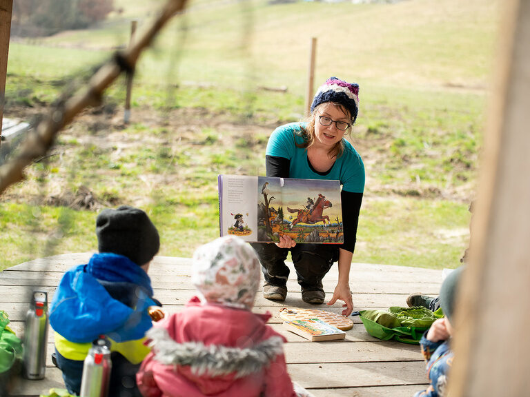 Kinderbetreuer zeigt Kinder Bilderbuch im Freien
