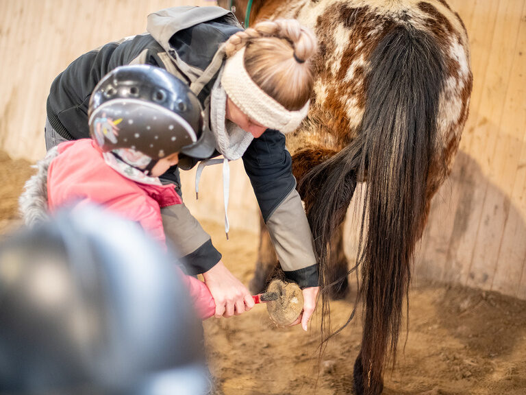 Reitlehrerin erklärt Kind wie man Hufe auskratzt