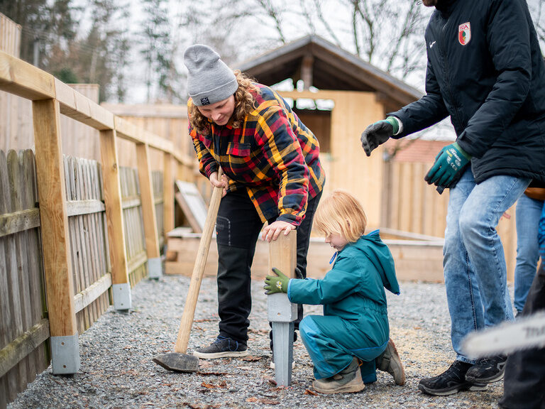 Eltern und ein Kind beim einschlagen einer Bodenhülse