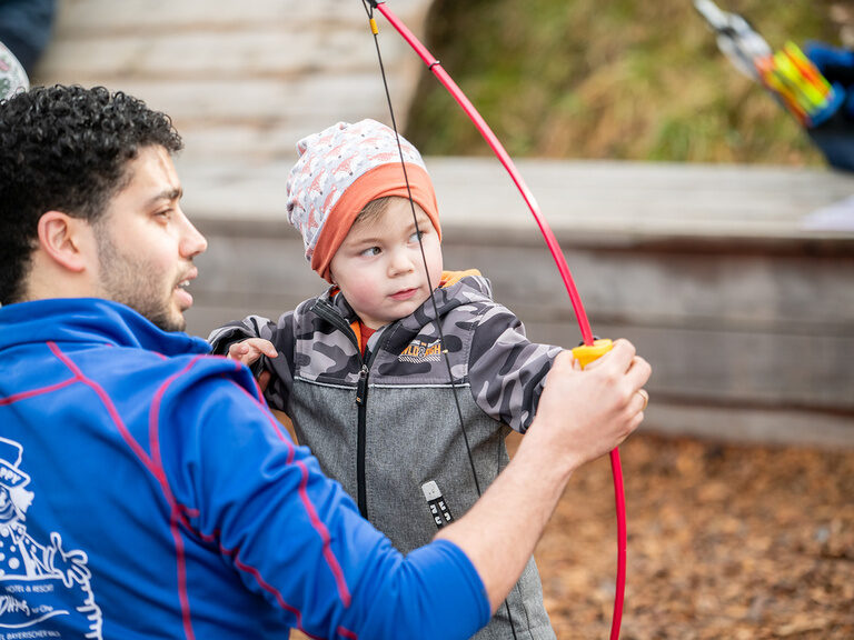 Kinderbetreuer erklärt Jungen wie er einen Bogen halten muss