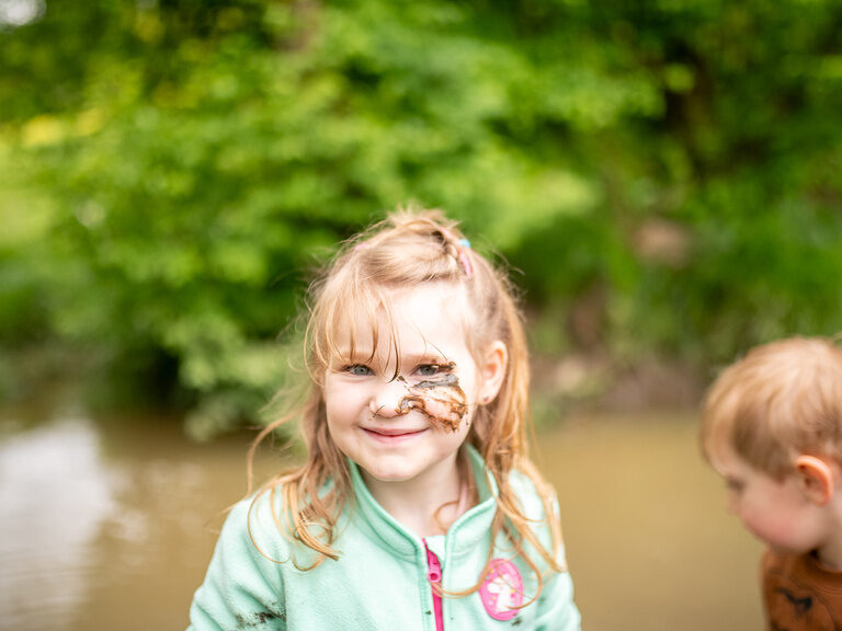 Kind mit Matsch im Gesicht am Bach