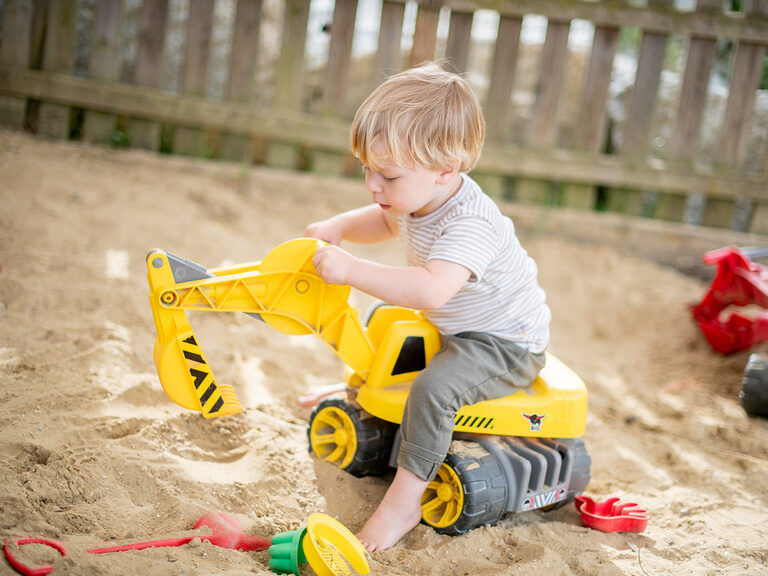 Junge sitzt auf Spielzeug Bagger im Sandkasten