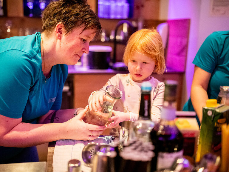 Kinderbetreuerin hilft Kind beim Kindercocktail mixen