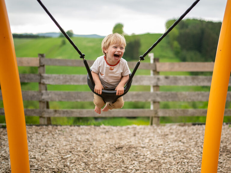 Junge in der Kleinkind schaukel jubelt vor Spaß