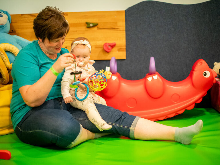 Baby sitzt auf dem Schoß einer Kinderbetreuerin und schaut auf Spielzeug