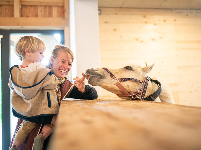 Mutter mit Kind auf dem Arm streichelt Pferd