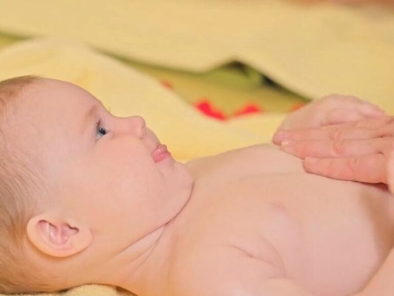 Baby liegt auf dem Rücken und wird über den Bauch gestreichelt