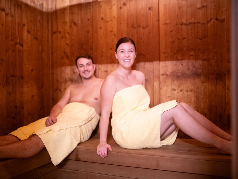Paar sitzt mit Handtüchern bedeckt in der Sauna