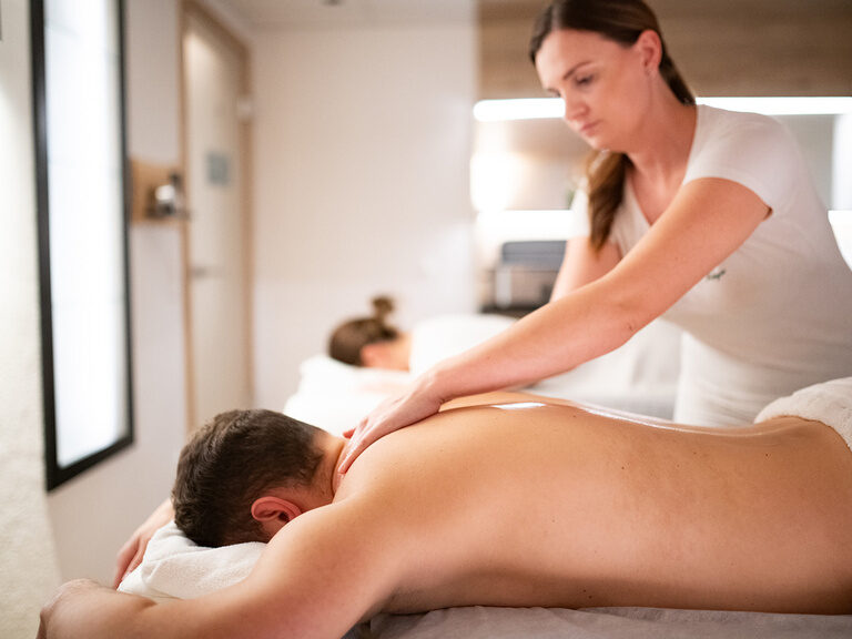 Frau und Mann liegen auf Massageliegen während der Mann von einer Masseurin massiert wird