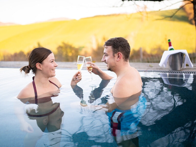 Pärchen im Outdoor Pool stößt mit einem Glas Sekt an