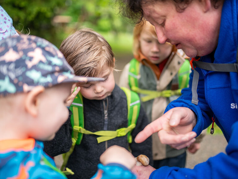 Frau mit Schnecke auf der Han umringt von Kindern
