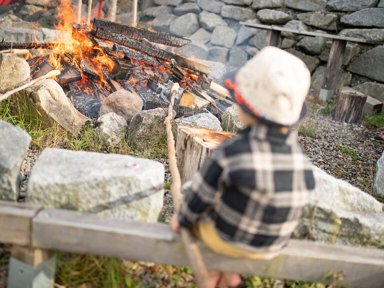 Junge sitzt am Lagerfeuer und backt Stockbrot