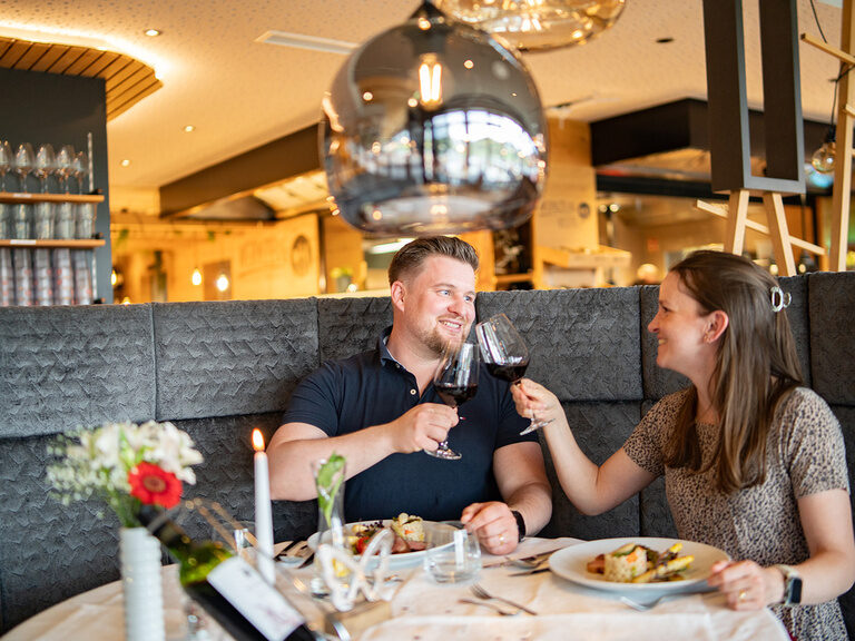 Mann und Frau sitzen an schön gedeckten Tisch und stoßen mit einem Glas Wein an
