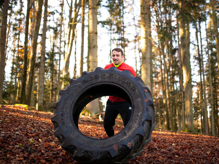 Mann im Wald beim "LandhausFit" hebt Traktorreifen an