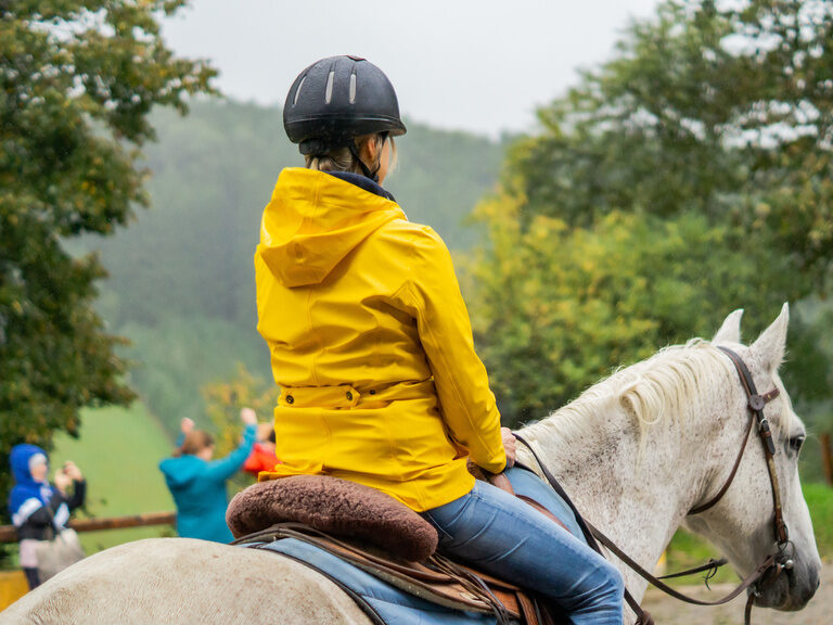 Frau im gelben Regenmantel bei Ausritt auf dem Pferd